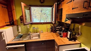 Cocina pequeña con ventana, muebles de madera y electrodomésticos básicos.