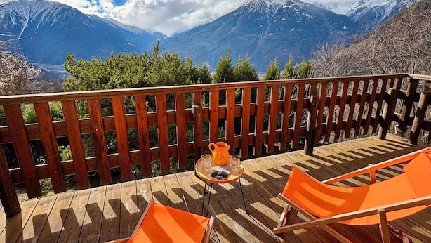 Una terraza de madera con una mesa, sillas y vistas a montañas nevadas.