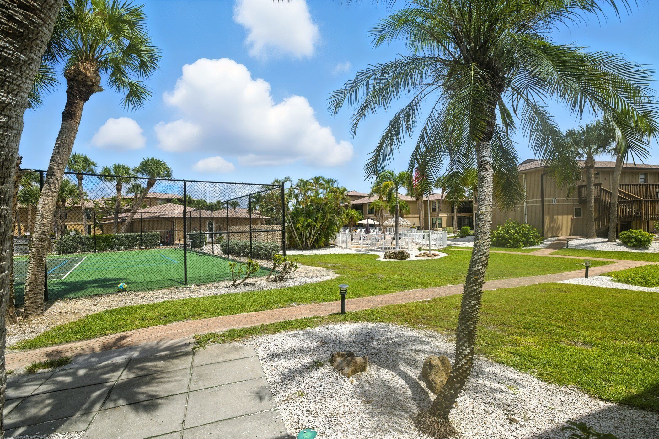 A courtyard with a tennis court, palm trees, and a building with a red roof.