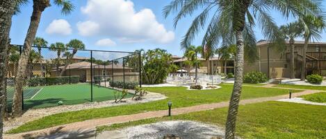 A courtyard with a tennis court, palm trees, and a building with a red roof.