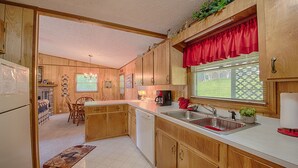 Une cuisine avec des meubles de rangement en bois, un évier, une machine à café et une fenêtre avec des stores.