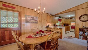 Un intérieur en bois comprenant une table à manger, des chaises, un lustre, un coin cuisine et une horloge murale.