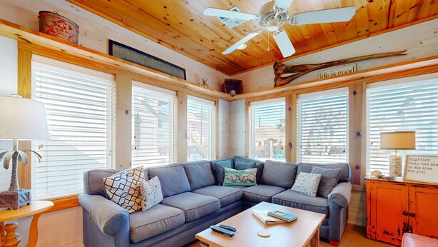 A cozy living room with a sectional sofa, a wooden coffee table, and a ceiling fan. - Spacious Home in Town, Back Patio, Shared Pool, Golf Cart Accessible (Port Aransas)