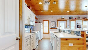 A modern kitchen with white cabinets, a central island, and wooden ceiling. - Spacious Home in Town, Back Patio, Shared Pool, Golf Cart Accessible (Port Aransas)