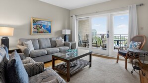 A living room with a sofa, coffee table, and chairs, a painting on the wall, and a balcony with outdoor furniture.