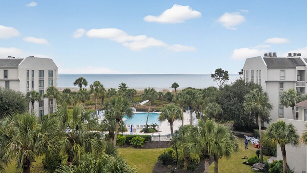 A resort with a pool surrounded by palm trees, overlooking a beach.