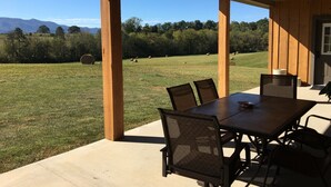 A covered patio with a table and chairs, overlooking a grassy field with hay bales and trees. - The Mockingbird Farm "Barn-do-minium" is situated on 27 rolling acres. (Seymour)