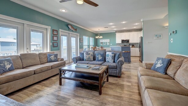 A spacious living room with a ceiling fan, a kitchen area, and a view of the ocean through large windows.