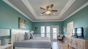 A bedroom with a bed, a ceiling fan, a TV, and a window.