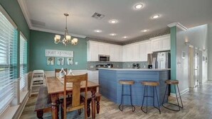 A modern kitchen with a central island, white cabinetry, and a dining area with a wooden table and chairs.