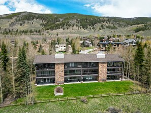 A modern hotel with a stone facade, multiple floors, and a view of surrounding mountains and houses.
