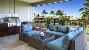 A balcony with a grill, wicker furniture, and a view of palm trees. - Breathtaking Luxurious Pacific Island Home (Waimea)