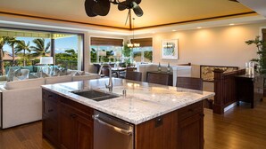 A modern kitchen with a large island, wooden cabinetry, and a view of the outdoors. - Breathtaking Luxurious Pacific Island Home (Waimea)