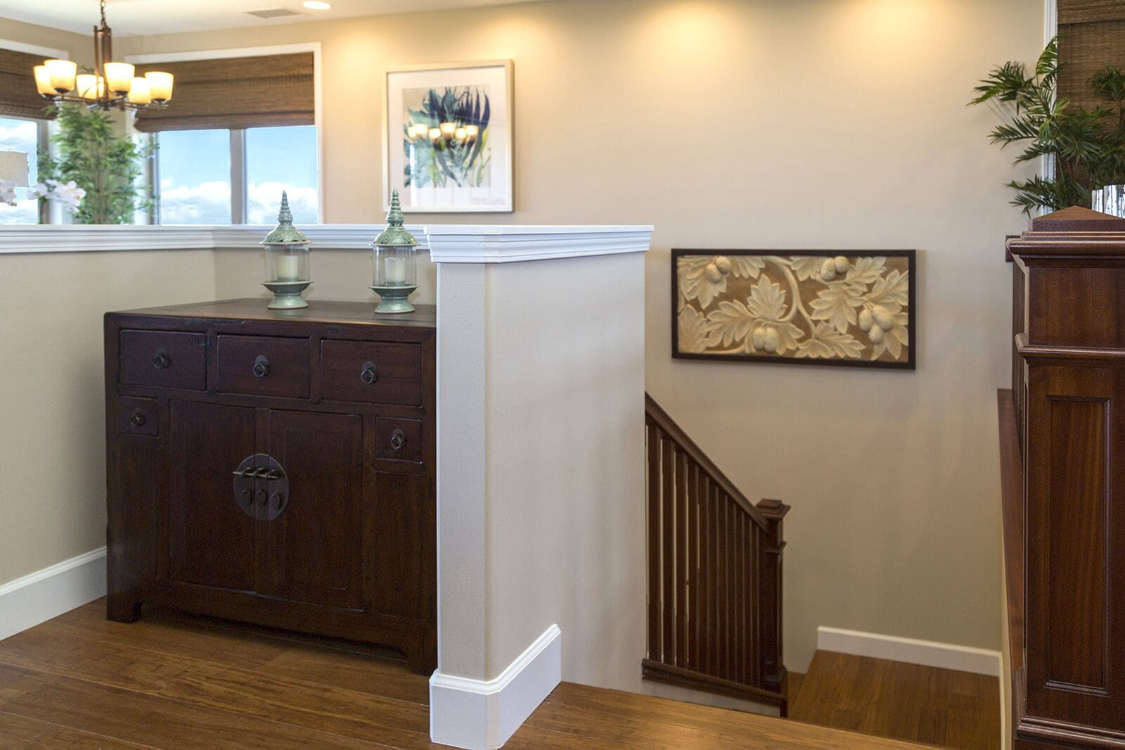 A wooden staircase with a handrail, a dark wooden dresser with multiple drawers, and a white baseboard.
