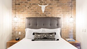 A bed with a tufted headboard, two bedside lamps, a white pillow, a patterned pillow, and a brick wall with a cow skull decoration. - Modern Surf-Inspired Bungalow with Epic Rooftop Views & Pool (Emiliano Zapata)
