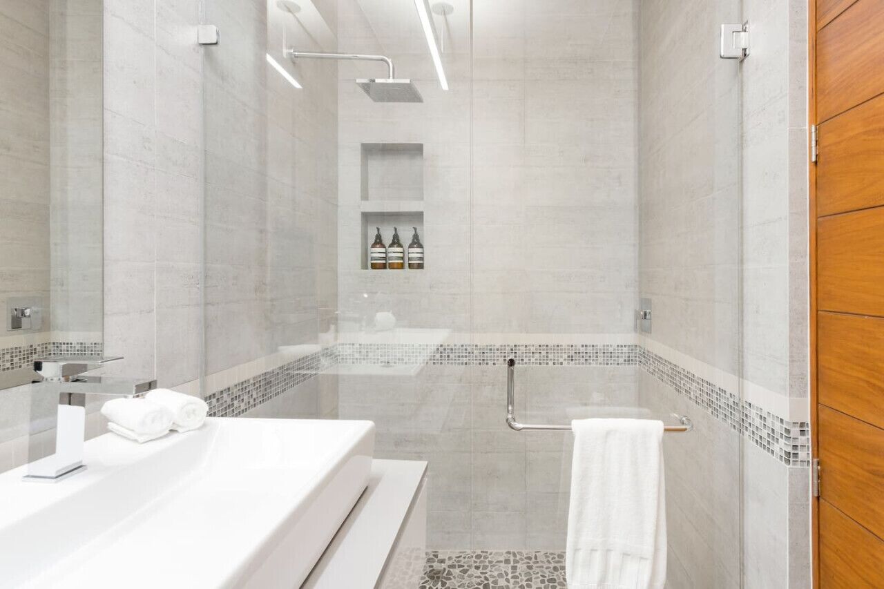 Un baño moderno con ducha envuelta en vidrio, lavamanos blanco y tocador de madera.