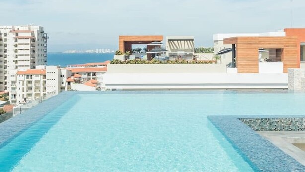 A rooftop infinity pool with a clear view of the sea and modern buildings in the background. - Modern Surf-Inspired Bungalow with Epic Rooftop Views & Pool (Emiliano Zapata)