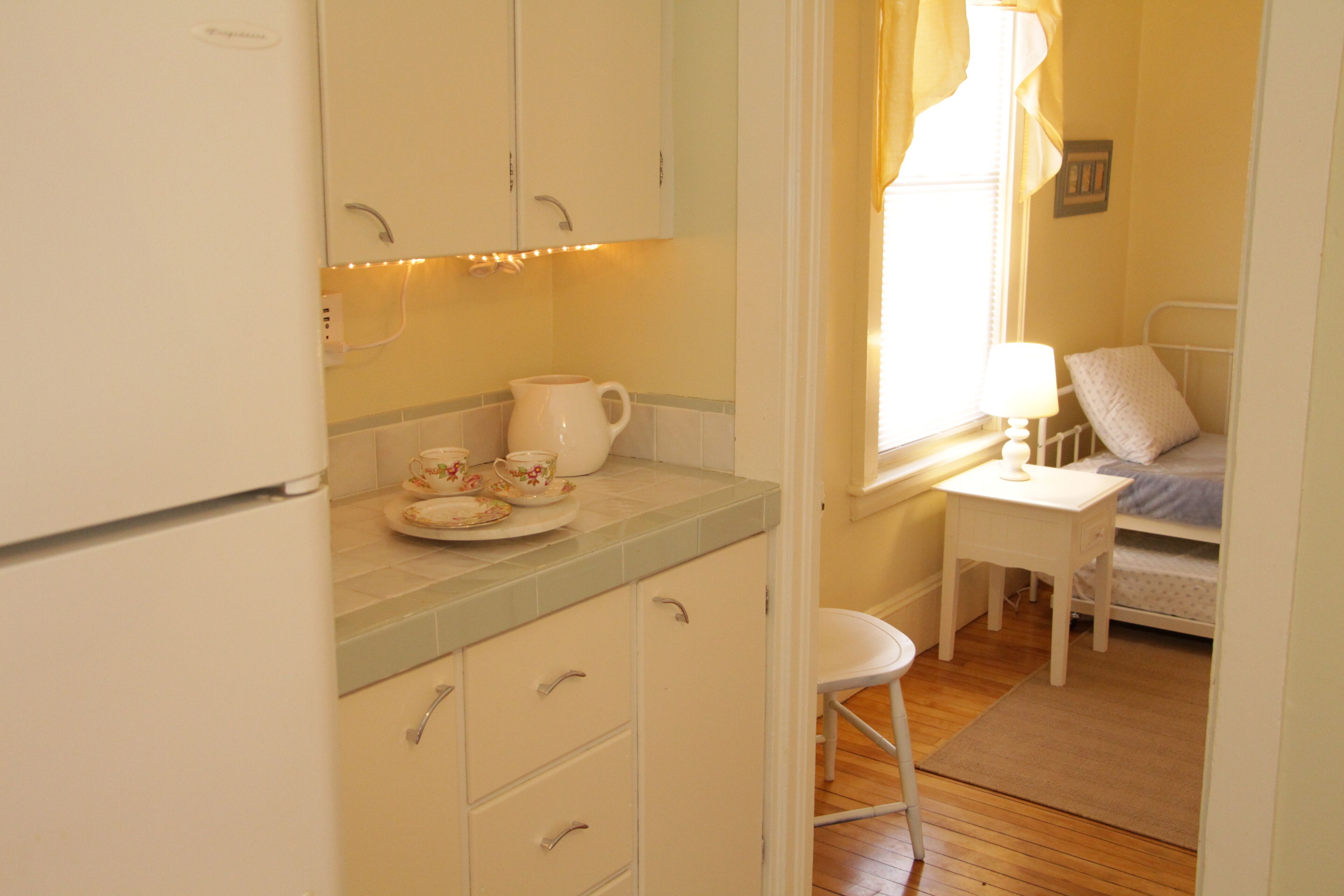 A small, cozy room with a kitchenette, a single bed, and a window with curtains.