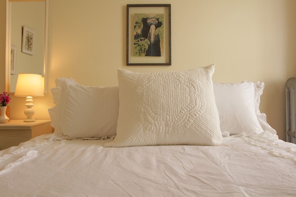 Un lit bien fait, avec du linge de lit blanc et des oreillers, une lampe de chevet et une œuvre d’art encadrée au mur.