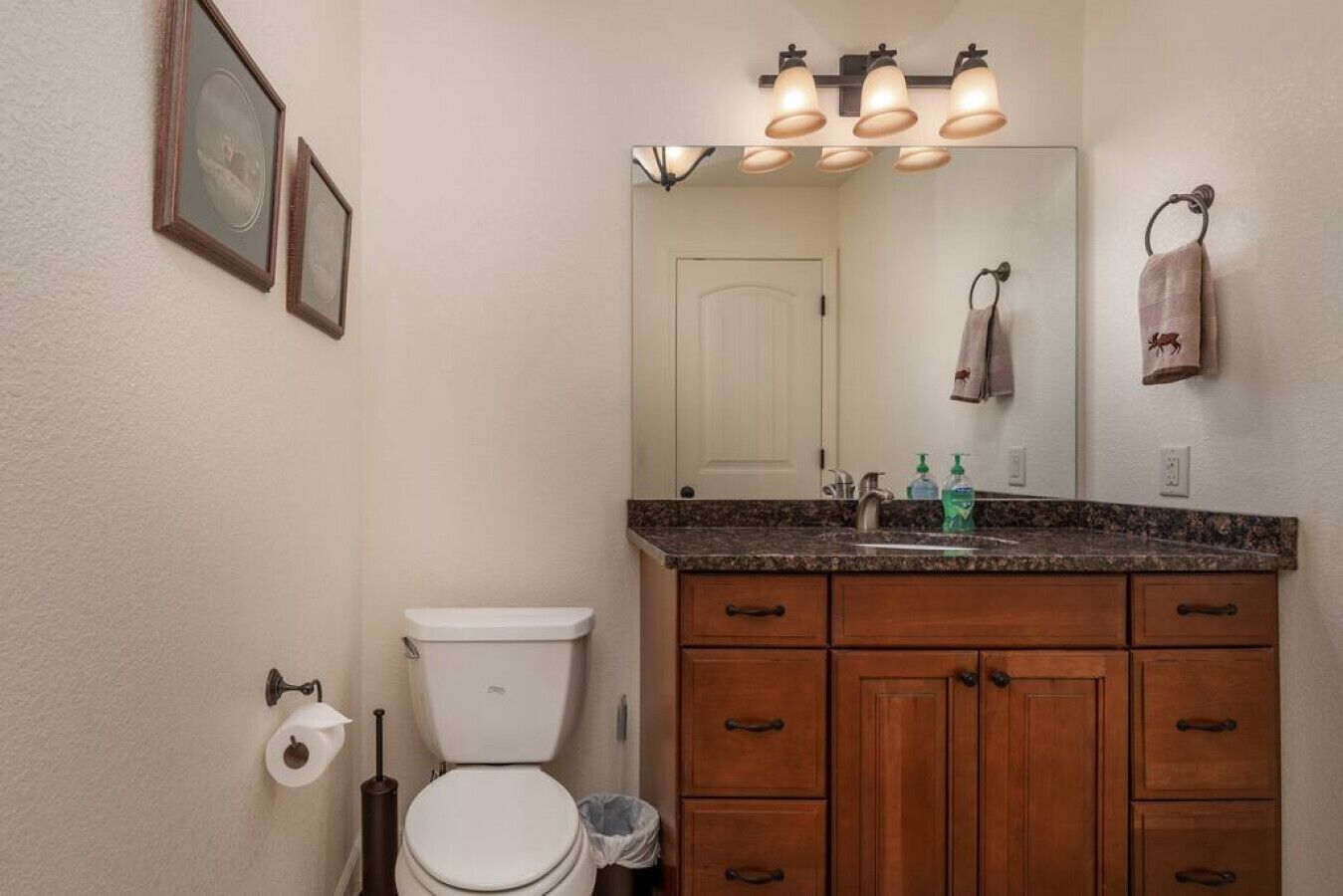 A bathroom with a toilet, a sink with a mirror above it, wooden cabinets, and a towel hanging on the wall.