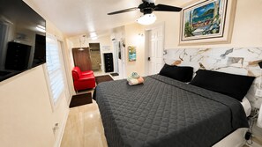 A bedroom with a bed, a ceiling fan, a painting, and a red chair.