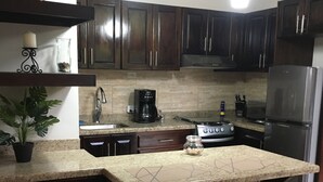 A kitchen with dark wood cabinets, a granite countertop, a stainless steel refrigerator, and a coffee maker.