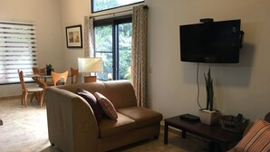 A living room with a sofa, a TV, a coffee table, and a dining area with chairs and a table.