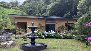 A modern building with a stone wall, a fountain, and a garden with hydrangeas.