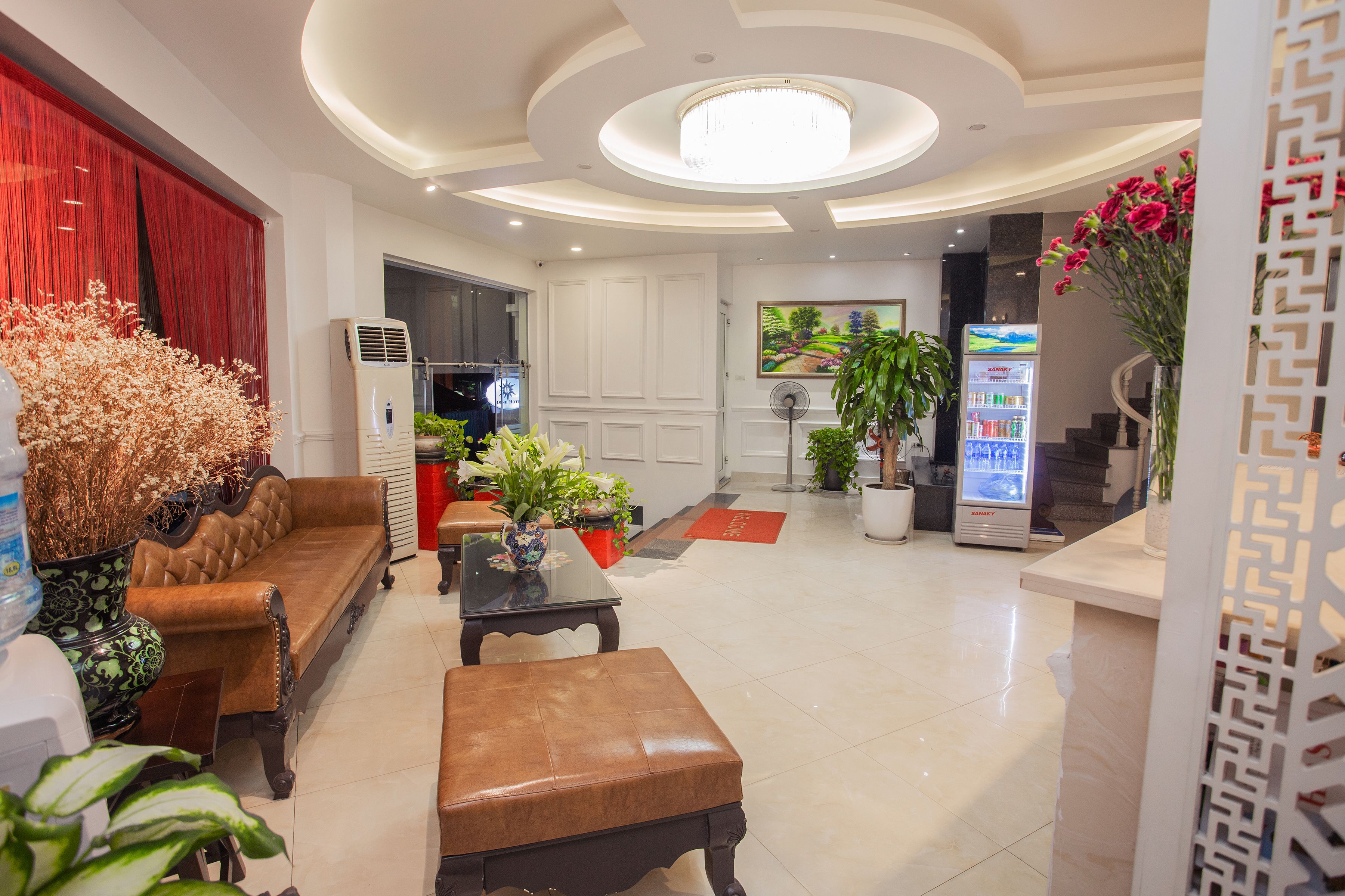 A modern hotel lobby with a brown leather sofa, a glass-top coffee table, a white reception desk, and a large chandelier.