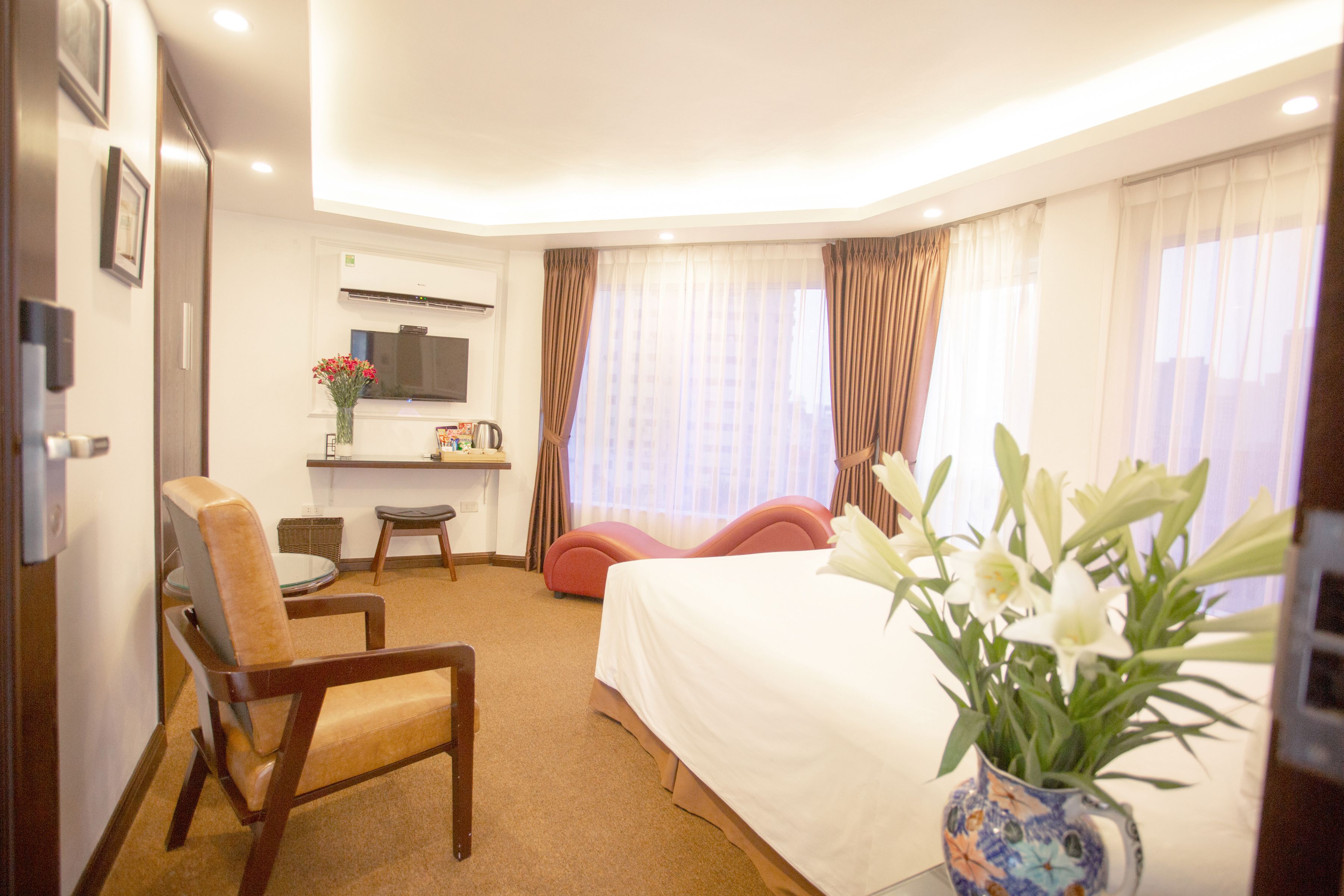 Une chambre d’hôtel avec un lit, un bureau, une chaise et un vase de fleurs.