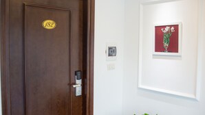 A wooden door with a number plate, a wall-mounted intercom, and a framed artwork of flowers. - Dinh Hotel (Hanoi)