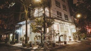 A hotel with a white facade, multiple windows, and a balcony. There are potted plants around the entrance. - Dinh Hotel (Hanoi)