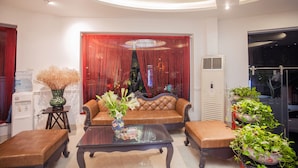 A modern living room with a brown leather sofa, a glass coffee table, and a red curtain backdrop. - Dinh Hotel (Hanoi)