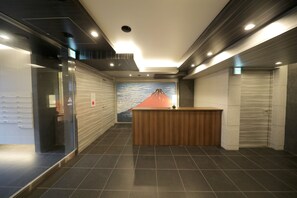 A modern reception area with a wooden reception desk, tiled flooring, and a mural of a mountain. - YOU-TRIP Oshiage Hotel (Tokyo)