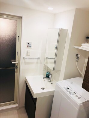 A bathroom with a white sink, a mirror, a toilet, and a washing machine. - YOU-TRIP Oshiage Hotel (Tokyo)