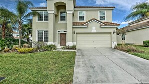 A two-story house with a garage, a front lawn, and palm trees.