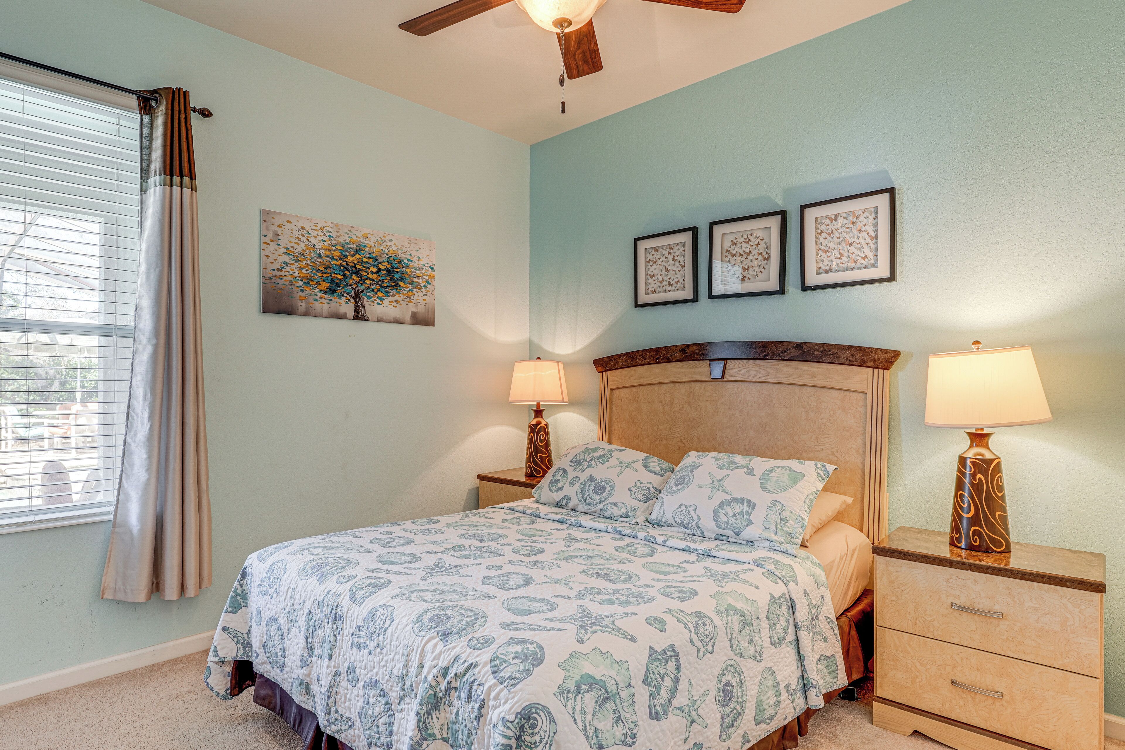 A bedroom with a bed, nightstands, a ceiling fan, and wall art.