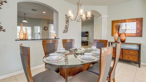 A dining area with a round glass table, six chairs, and a chandelier.