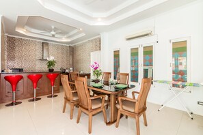 A modern kitchen with a dining area, featuring a large island with stools, wooden chairs, and a glass-top table.