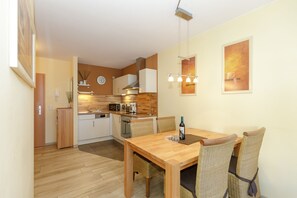 A modern kitchen with white cabinets, a wooden countertop, and a dining area with wicker chairs and a wooden table. - Apartment near the beach at the marina (Kühlungsborn)