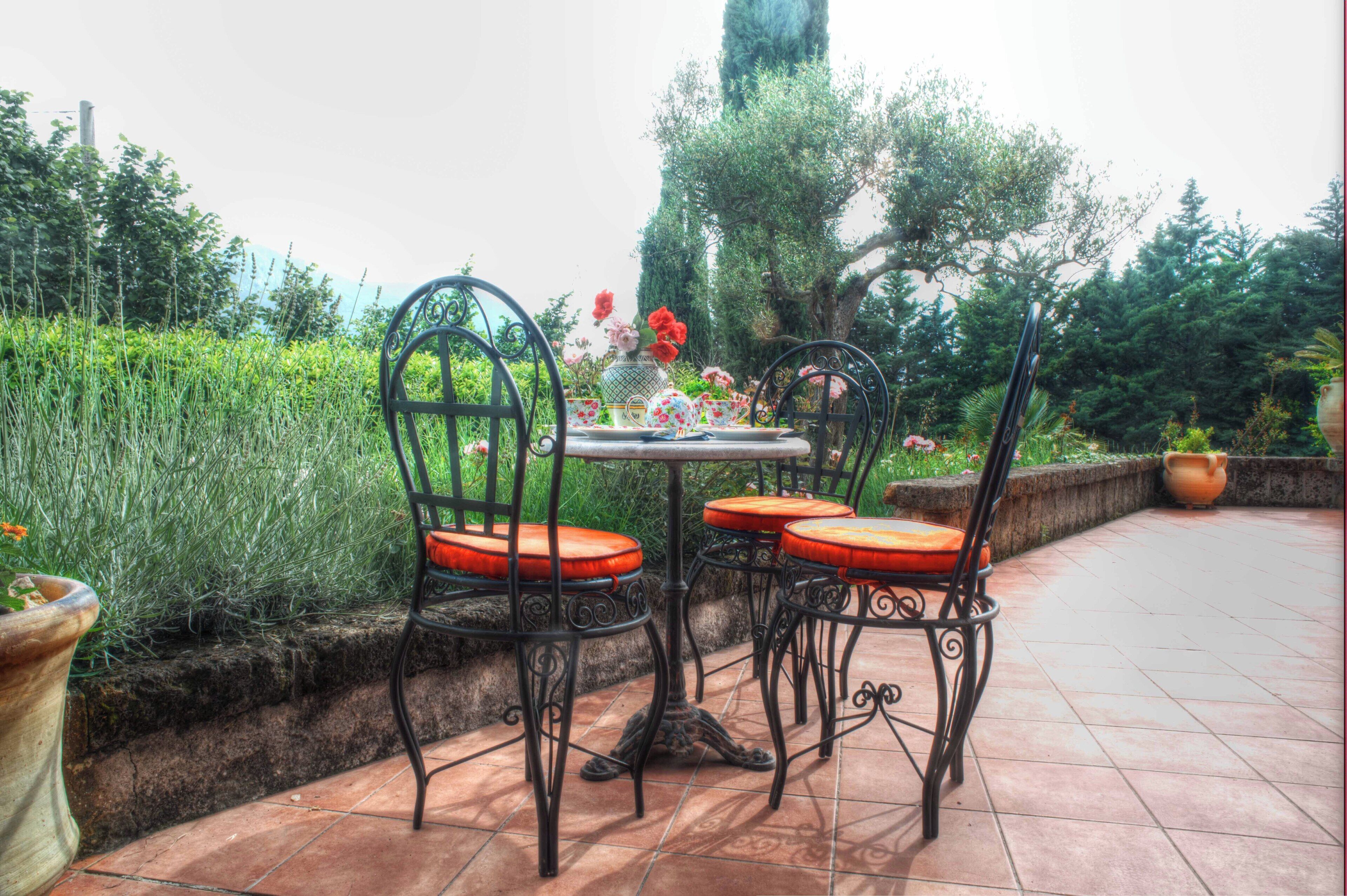 Une terrasse avec une table ronde et quatre chaises, entourée d’une végétation luxuriante et d’un mur de pierre.