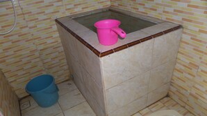 A small bathroom with a toilet, a blue bucket, and a pink basin on a tiled floor. - Villa Anna (Ngadisari)