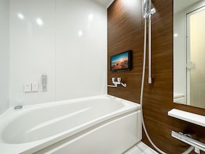 Un baño moderno con una bañera blanca grande, un revestimiento de madera, un televisor montado y un espejo.