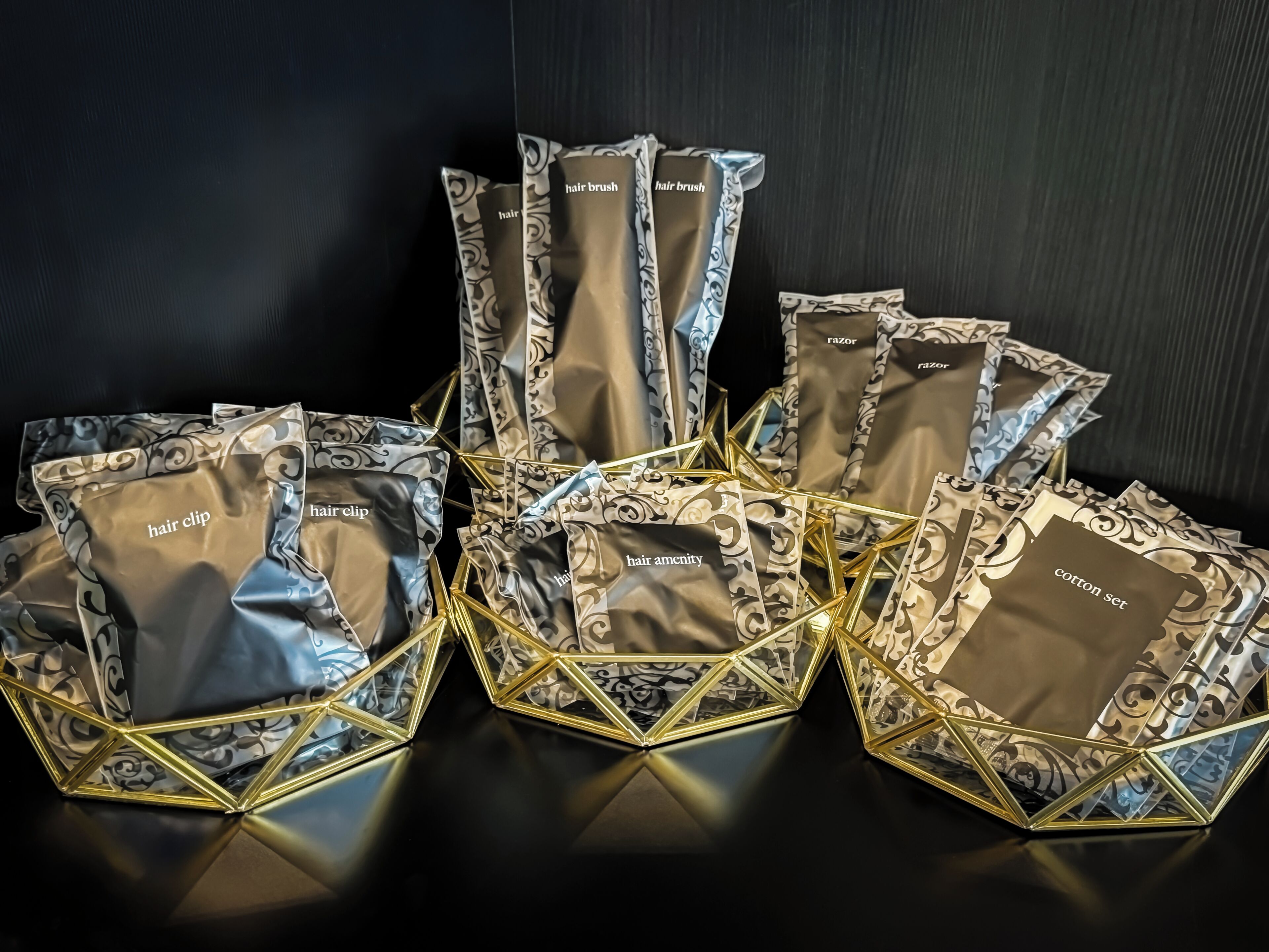 Exposição de sacolas de presente com diversos itens etiquetados, dispostos em um padrão geométrico sobre uma superfície refletora.