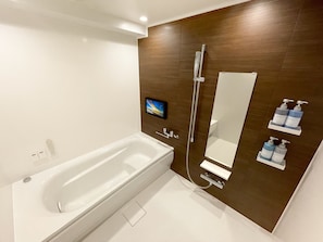 A modern bathroom with a large bathtub, a wall-mounted TV, and a mirror. - Hotel 31 (Funabashi)