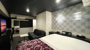 Quarto de hotel moderno com uma cama grande, uma escrivaninha, uma cadeira, uma televisão e um detalhe decorativo na parede.