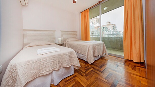 Ein Hotelzimmer mit zwei Betten, Holzboden und Blick auf die Stadt durch große Fenster.