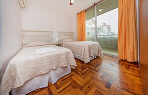 A hotel room with two beds, wooden flooring, and a view of the city through large windows. - Rent Obispo Trejo JW4 (Córdoba)
