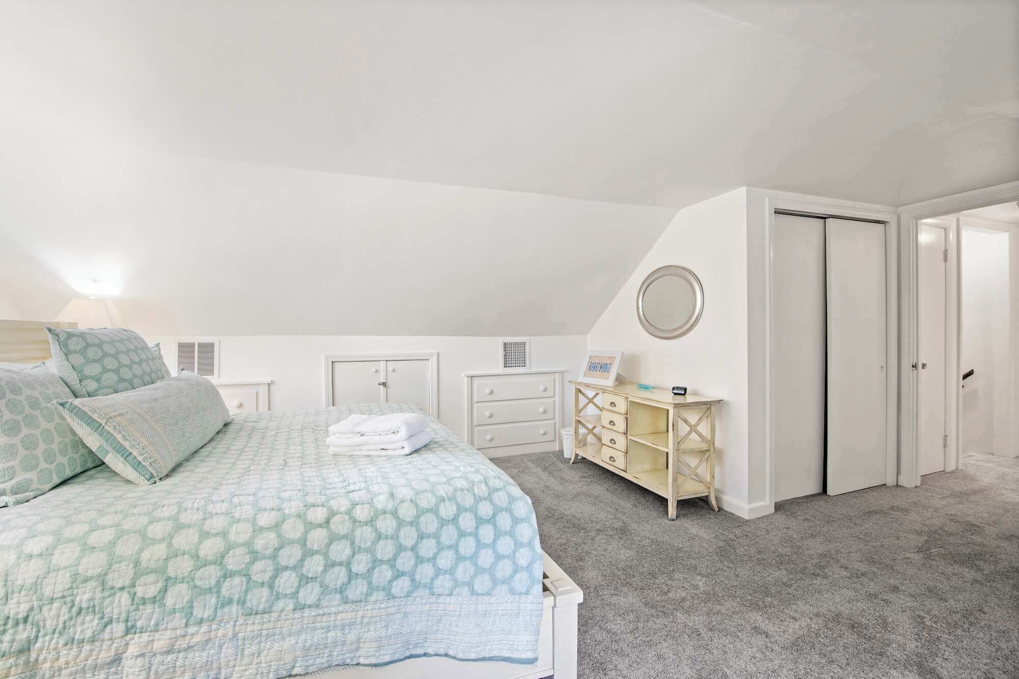 A bedroom with a bed, a dresser, a mirror, and a door.