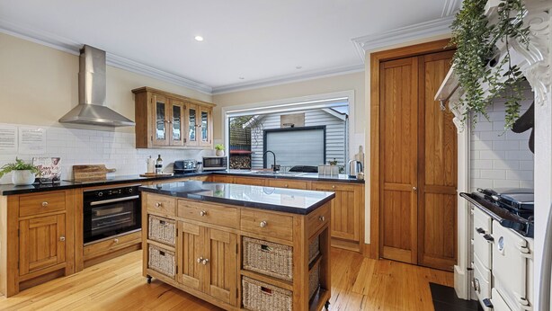 Une cuisine moderne avec des meubles en bois, un grand îlot central, des appareils électroménagers en acier inoxydable et une vue sur le jardin.
